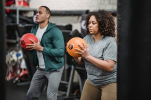 Concentrated young diverse trainer and athlete exercising with medicine balls in gym